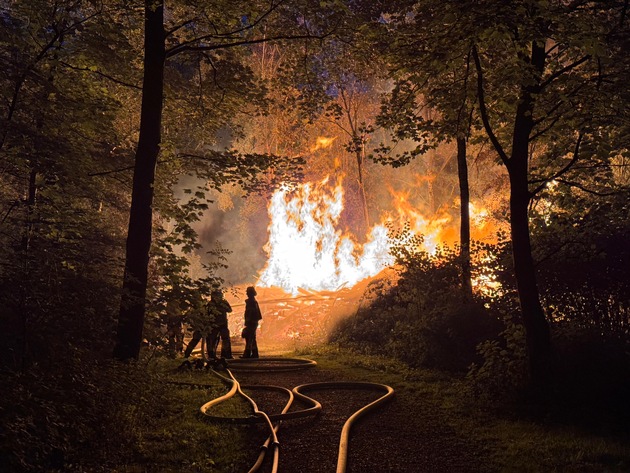 FW-E: Großer Holzstapel geht in Flammen auf - Feuerwehr verhindert Ausbreitung auf angrenzenden Wald